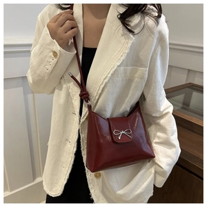 Détail du sac sous l'aisselle en cuir verni bordeaux avec nœud argenté sur blazer blanc