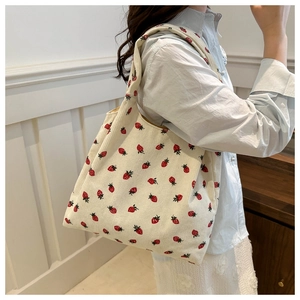 Detail of strawberry print tote bag in cream corduroy fabric worn by a female model