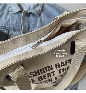 Detail shot of a smooth white zipper closure on a beige canvas tote bag with black lettering