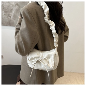 Chic white pleated crescent bag with bow detail and ruffled shoulder strap on model