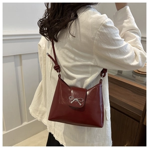 Side view of wine red glossy shoulder bag with silver bow accent on model