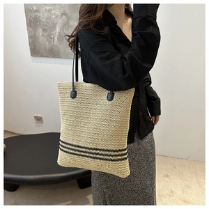 Detail of a beige woven straw tote bag featuring black stripes and slim leather straps