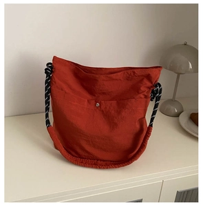 Gros plan sur un sac seau orange en nylon avec bouton pression et bandoulière corde