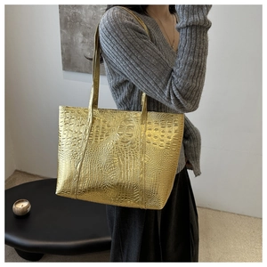 Detail of gold tote bag featuring premium crocodile embossed texture and long shoulder straps