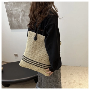 Detail of a woven straw tote bag with black stripes and long shoulder straps on a model