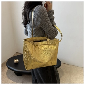 Detail view of large gold tote bag with embossed crocodile pattern and dual handles