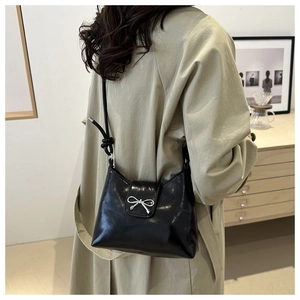 Detail of black leather underarm bag with silver bow on beige trench coat model