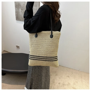 Detail view of woven straw tote bag featuring black stripes and slim leather straps