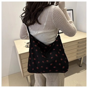 Close-up of black corduroy tote bag with red strawberry pattern and shoulder strap
