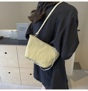 Detail of cream shoulder bag featuring pleated texture and golden chain strap for women