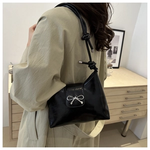 Détail d'un sac à bandoulière noir brillant avec boucle noeud argentée et bandoulière nouée