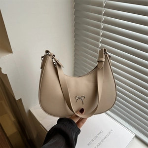 Minimalist beige crescent underarm bag with a silver bow detail on a white windowsill
