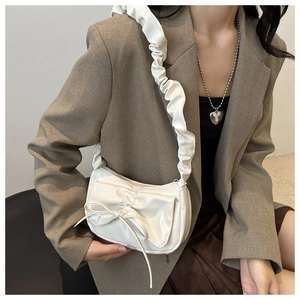 Close-up of stylish white shoulder bag featuring a large bow and pleated strap detail
