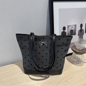 Grey polka dot tote bag with black leather straps and silver bow charm on a table