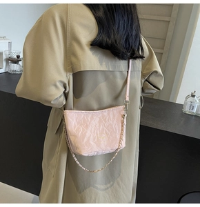 Pink crossbody bag with pleated texture and chain strap worn over a khaki trench coat
