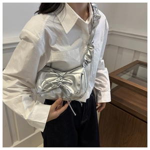 Detail of silver metallic shoulder bag featuring bow knot and ruffled wide strap design