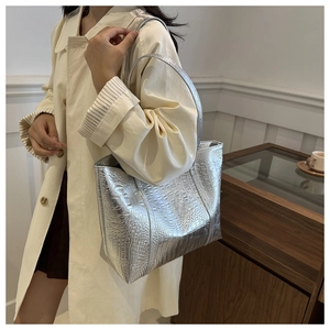 Detail of silver crocodile pattern tote bag shown by model in minimalist interior
