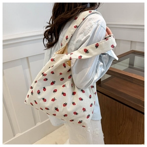 Close-up of white corduroy tote bag with red strawberry print on striped texture fabric