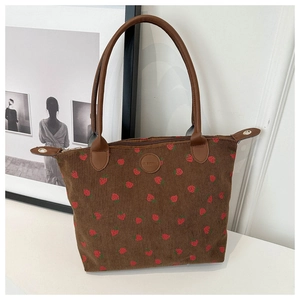 Detail of corduroy tote bag featuring red strawberry prints and premium brown leather handles