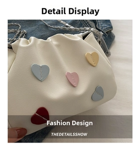 Detail of off-white dumpling bag with colorful heart patches and silver chain strap
