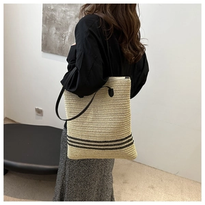Detail of straw tote bag showing beige woven texture with black horizontal stripes