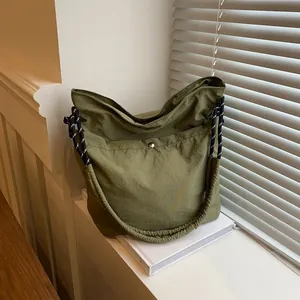 Sac fourre-tout minimaliste vert armée avec bandoulière tressée posé sur des livres