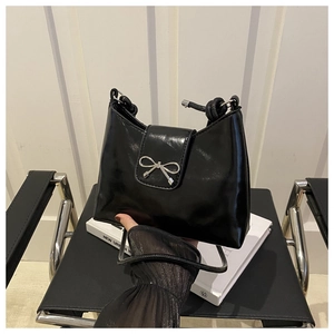 Detail of black glossy shoulder bag featuring a silver metal bow clasp and knotted strap