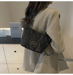 Detail of black wrinkled texture baguette bag with golden chain strap and brand logo