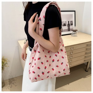 Detail of pink corduroy tote bag with strawberry prints worn over the shoulder