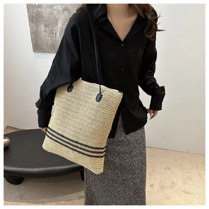 Detail of hand-woven straw bucket bag with black stripes and leather straps