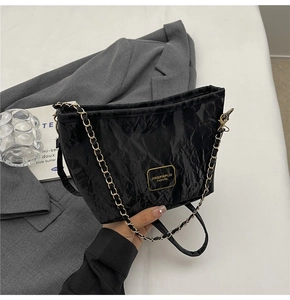 Detail of black wrinkled texture bucket bag with gold chain strap and metal logo plate