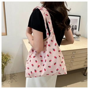 Lifestyle view of a pink corduroy tote bag with strawberry print and wide shoulder strap