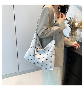 Detail of white canvas tote bag with black bow print worn with a beige blazer