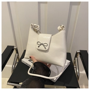 Close-up of white bucket bag with silver bow clasp and knotted strap detail on black chair