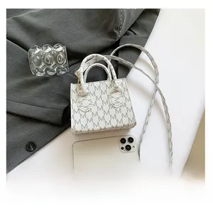 Close-up of cream shoulder bag with grey M-letter print and gold metal hooks