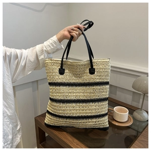 Detailed close-up of large straw tote bag with black stripes on a wooden table