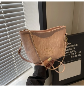 Detail of pink drawstring bucket bag featuring pleated texture and gold chain strap