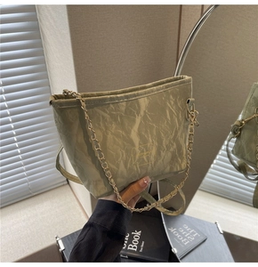 Close-up of light green pleated bucket bag with gold chain strap in a lifestyle setting
