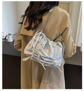 Détail du sac argenté plissé avec nœuds et bandoulière chaîne sur manteau kaki