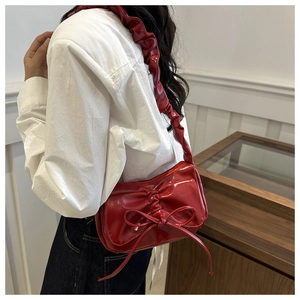 Detail of red patent leather shoulder bag with pleated bow and ruffled strap design