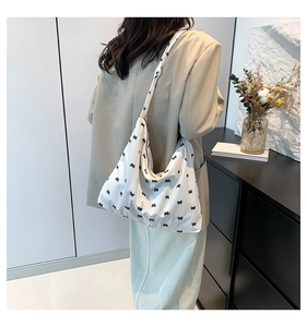 Detail of white canvas tote bag featuring black bow patterns and soft wide shoulder strap