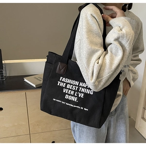 Detail of black canvas tote bag showing side pocket and stylish letter print for students