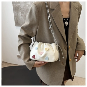 Detail of cream drawstring bucket bag with colorful heart patches and metal chain strap