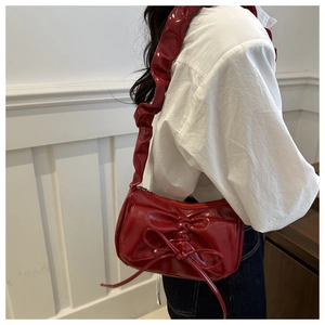 Red glossy patent leather shoulder bag with bow detail and pleated strap on model