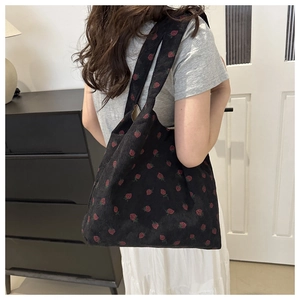 Detail of strawberry print on black corduroy tote bag worn by model in home setting