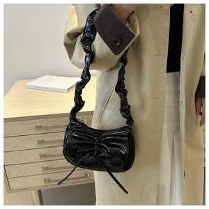 Detail showing glossy black underarm bag with pleated bow and scrunchie shoulder strap