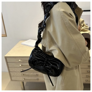 Detail of black patent leather shoulder bag with oversized bow and ruffled strap