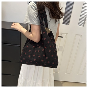 Detail of strawberry embroidery on black corduroy tote bag worn over the shoulder