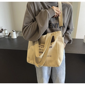 Detail of beige canvas tote bag showing side storage pocket and black artistic lettering