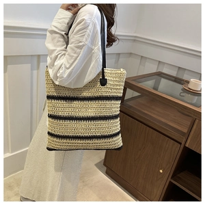 Detail of hand-woven straw tote with brown horizontal stripes and black leather straps